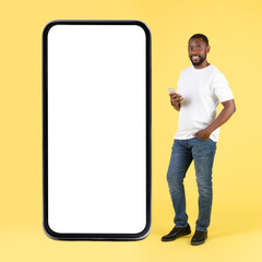 African Male Using Phone Standing Near Huge Smartphone In Studio