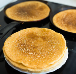 hot golden pancakes made from grain flour in kitchen while cooking on pans and on plate