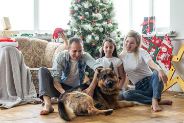 smiling family and daughter with dog sitting near christmas tree with gifts