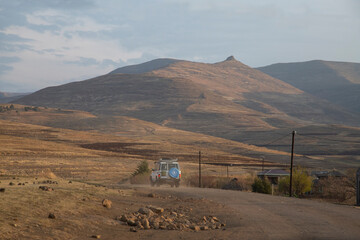car driving on dirt road with sun setting through mountains 