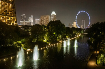 Singapore, July 24, 2022 - Water fountains on canal with ferris wheel in background at night.