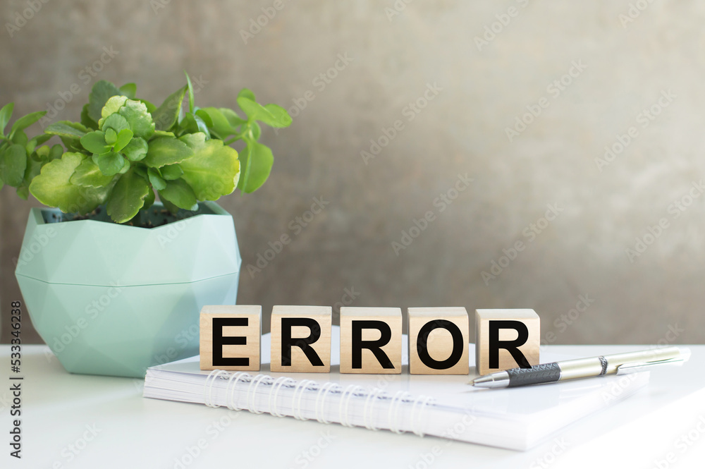 Aufkleber error text on wooden cubes on a table side by side a notebook, a pen and a flower in a pot