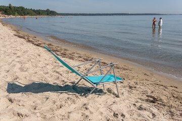 A folding chair on the beach facing the sea. Warm sunny day. Symbol of holidays, leisure.