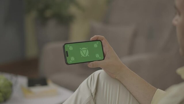 Man watching and touch iPhone 14 green screen mock-up on sofa chilling in home, Horizontal , camera tracking September 2022 - Berlin, Germany 