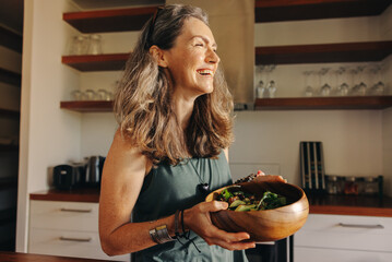 Aging woman smiling happily while holding a buddha bowl - obrazy, fototapety, plakaty