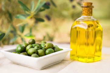 still life of olives and oil on a table against a background of olive trees