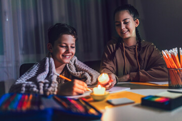 Boy and girl studying in low light with a burning candle.  Power outage, energy crisis concept.