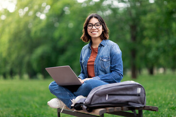 Happy Middle Eastern Female Student Sitting On Bench Outdoors With Laptop