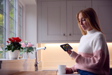 Worried Woman Looking At Smart Meter In Kitchen At Home During Cost Of Living Energy Crisis