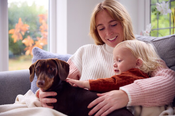 Mother With Son Sitting Under Blanket With Pet Dog During Cost Of Living Energy Crisis