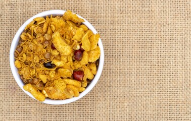 Top View of Spicy Chanachur in White Bowl Isolated on Burlap Fabric Background with Copy Space, Morning Snack
