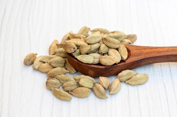 Dry Cardamon or Cardamom Pods in a Wooden Ladle Isolated on White Wooden Background