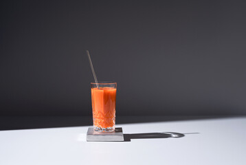 Vaso de jugo de zanahoria servido con una pajita sobre fondo gris	