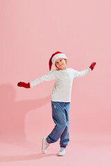 Obraz premium Emotional charming girl, child in casual style clothes, knitted mittens and Christmas hat having fun over pink background. Christmas, New Year, dreams, holidays