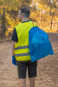 Hombre guardabosque de espaldas, con la bolsa de basura llena de pl&aacute;sticos. Fotograf&iacute;a vertical con copy space.
