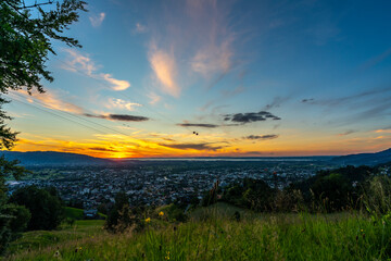 Fototapeta premium Sonnenuntergang über den Schweizer Bergen im Rheintal, Vorarlberg, Austria. leuchtendes Abendrot, tolle Stimmung mit roten und graublauen Wolken über den grünen Wiesen und Bäumen. Seilbahn zum Karren