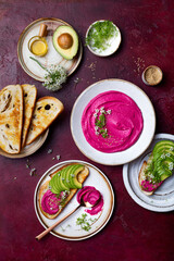 Avocado toast with pink beet hummus spread or dip with edible onion flowers and microgreens. Healthy plant based appetizer, vegan, vegetarian snack