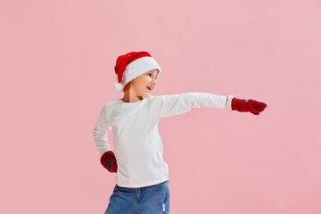 Dance. Cheerful little girl, child in casual style clothes, knitted mittens and Christmas hat having fun over pink background.