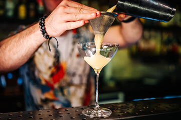bartender pouring cocktail in glass on the bar counter