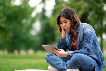 Fototapeta premium Bored Middle Eastern Female Student Sitting With Digital Tablet On Bench Outdoors