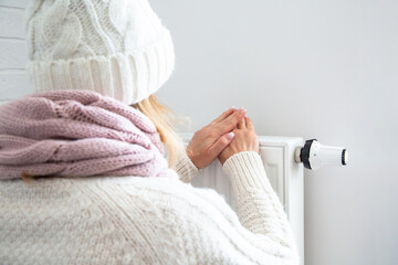 A woman warms her hands near the battery. Woman dressed warmly cold in the house. Saving heating....