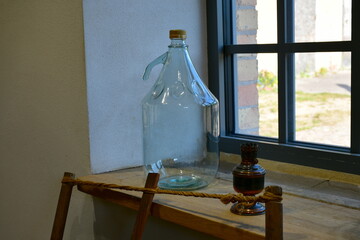 A close up on an old glass bottle with a handle and a cap used in the past to transport milk or water, seen on a windowsill of an old house on a sunny summer day in Poland 