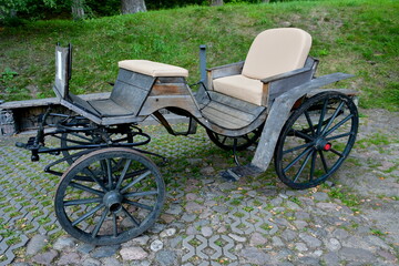 A close up on a wooden ancient cart or carriage with wooden wheels and body, as well as with leather finishing on the seats seen on a sunny summer day on a Polish countryside