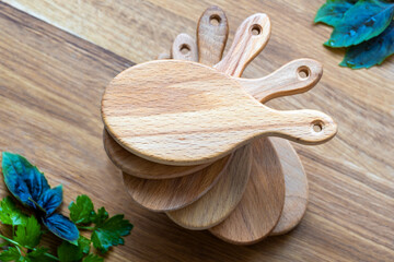 Serving wooden boards in drop shape, holes for hanging, stacked one another as spiral staircase, purple-green basil, parsley sprigs. Abstract food tableware design,natural backdrop, timber handmade