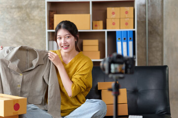 Pretty Asian online business owner going live selling clothes online explaining product features, price and usability.