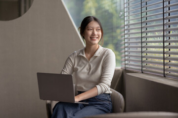 Fototapeta premium Cute and attractive Asian woman using laptop to work in a coffee shop happily and comfortably.