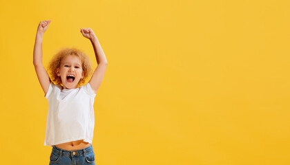 Fototapeta Thrilled little girl, kid shouting in rejoice and raising hands up isolated over yellow background. Concept of children positive emotions obraz