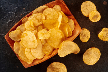 Potato chips or crisps, a salty snack in a bowl, overhead flat lay shot on a black slate background