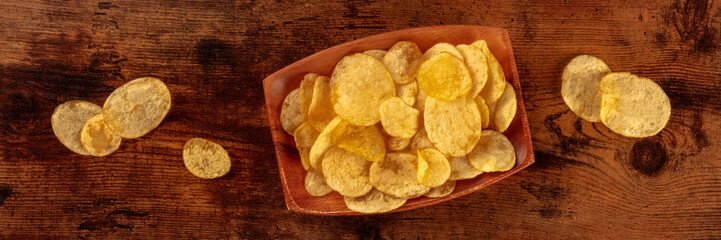Potato chips or crisps, a salty snack, overhead flat lay panoramic banner, on a wooden background