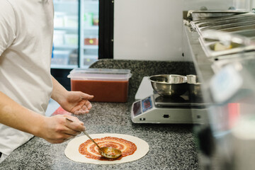 The process of making real Italian pizza. The chef prepares pizza and spreads tomato sauce on cake....