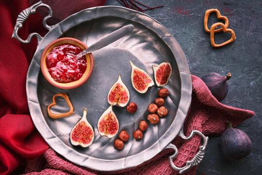autumntime background. Fresh halved fig fruits on elegant vintage zink plate or tray. Magenta towel, red scart on grey textured board. Vibrant Fall colors.