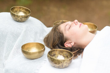 Young woman laying on a massage bed with tibetan singing bowl outdoor. Nepal copper singing bowl sound massage