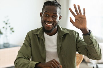 Greeting concept. Friendly black man waving at camera and smiling, saying hi while having video call at home © Prostock-studio