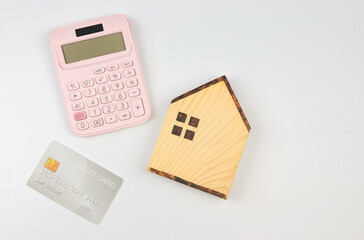 flat layout of wooden house model , pink calculator and credit card on white background with copy space.  home purchase concept.