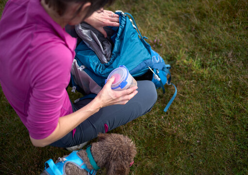 A female hiker packing their pet dogs dinner so they can feed them while out on a long walk in the countryside in England, UK.