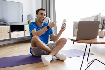 Workout application. Happy male fitness blogger showing smartphone to laptop webcam, recommending app for training