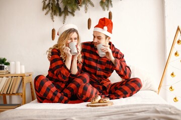 Couple wearing christmas plaid red pajamas sitting on the bed