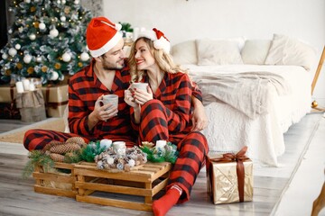 Couple wearing christmas plaid red pajamas sitting on the floor