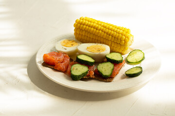 Breakfast plate on white texture background. Fish, eggs, cucumbers and corn.