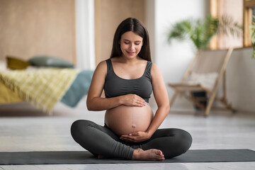 Maternity Concept. Young Pregnant Female Sitting On Yoga Mat And Embracing Belly