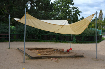 there is a tarpaulin between two wooden pillars. roof serving as a shading for the sandpit or...