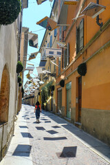 Parma, Italy: borgo Giacomo Tommasini, city street on a sunny day decored with mirrors. A girl walking in shadows. Narrow street of old town