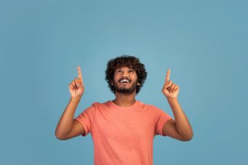 Cheerful hindu guy pointing at copy space on blue