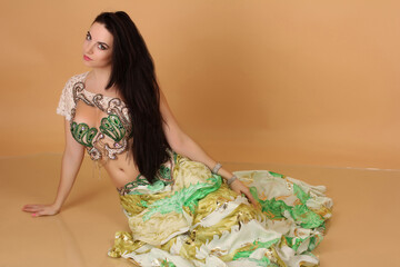 a pretty girl brunette who dances go-go and belly dance, stretching posing in studio in green arabian dress on a beige background