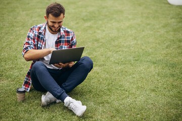 Man student sitting on grass and working on laptop