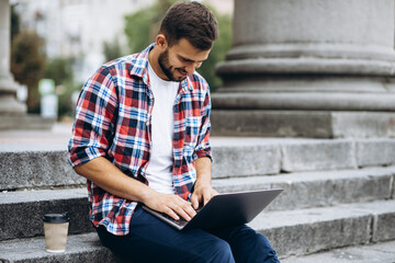 Man sitting on stairs drinking coffee and working on laptop